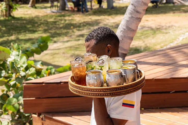 Servicekraft trägt im Freien in tropischer Umgebung ein Tablett mit erfrischenden Eis-Cocktails