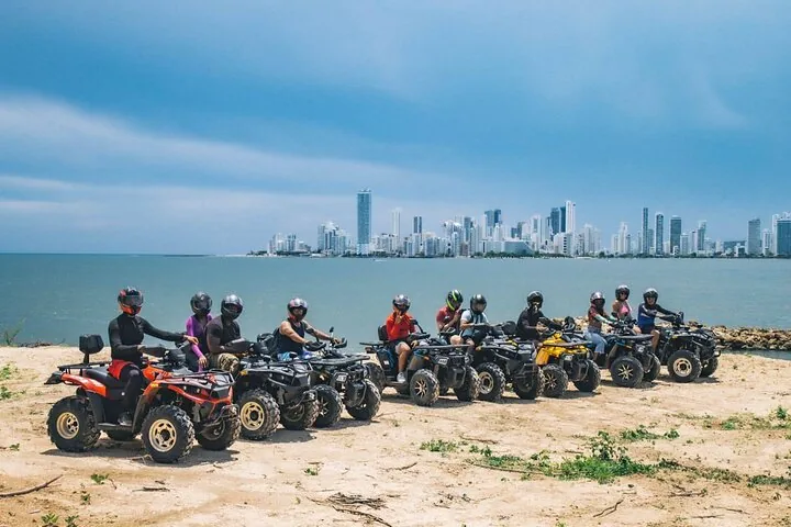 Group of people on ATVs lined up on a beach facing the city.