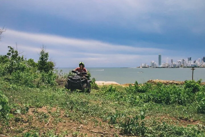 Person, die auf einem grasbewachsenen Hügel ein Quad fährt und auf eine ferne Stadt blickt.