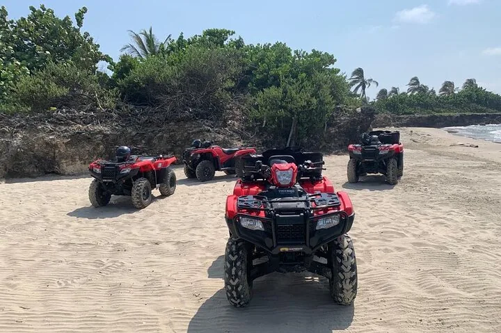 Vier rote Quads, geparkt an einem Sandstrand direkt am Ozean.