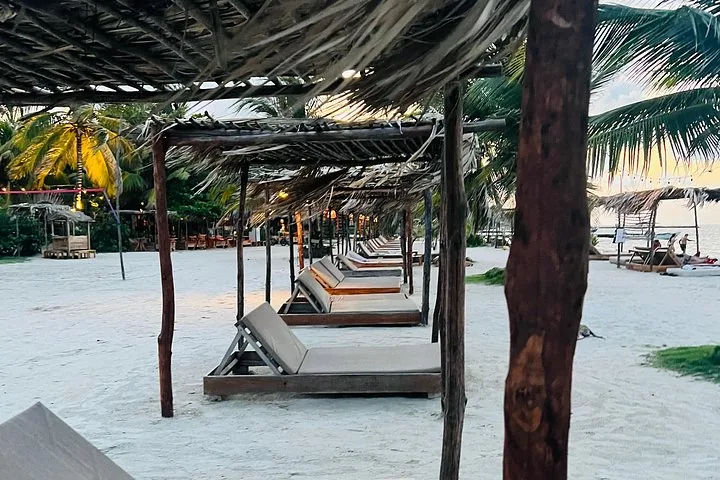 Liegestühle unter Strohschirmen an einem weißen Sandstrand