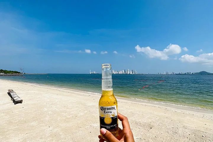 Person holding a bottle of Coronita beer on a sunny beach