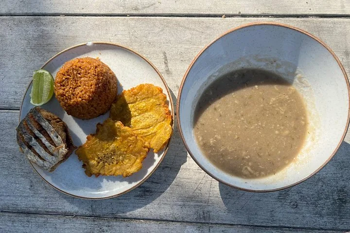 Ein Teller mit Fisch, Reis und Kochbananen neben einer Schüssel Suppe